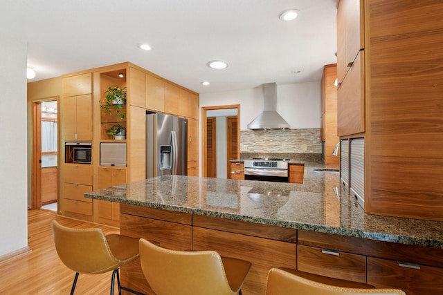 10933 Chowen Ave S, Bloomington, MN 55431 - kitchen featuring stainless steel appliances, wall chimney exhaust hood, backsplash, a peninsula, and dark stone countertops