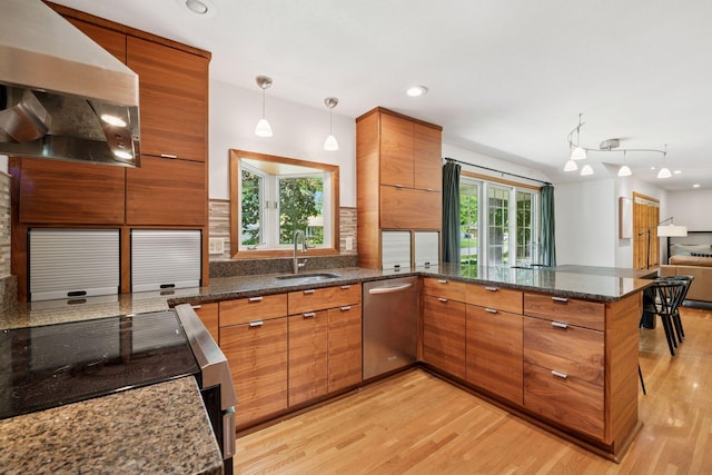 10933 Chowen Ave S, Bloomington, MN 55431 - kitchen with stainless steel appliances, a sink, wall chimney exhaust hood, brown cabinetry, and a peninsula