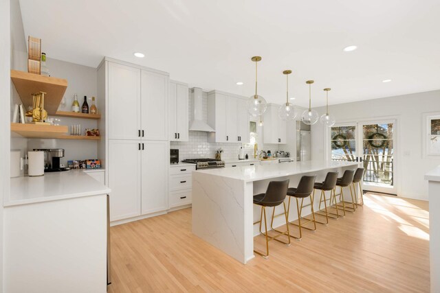 150 1st St, Excelsior, MN 55331 - kitchen featuring wall chimney range hood, light wood-type flooring, backsplash, a kitchen breakfast bar, and appliances with stainless steel finishes