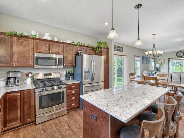 6024 158th St W, Apple Valley, MN 55124 - kitchen featuring stainless steel appliances, light wood-type flooring, a kitchen breakfast bar, decorative light fixtures, and light stone counters