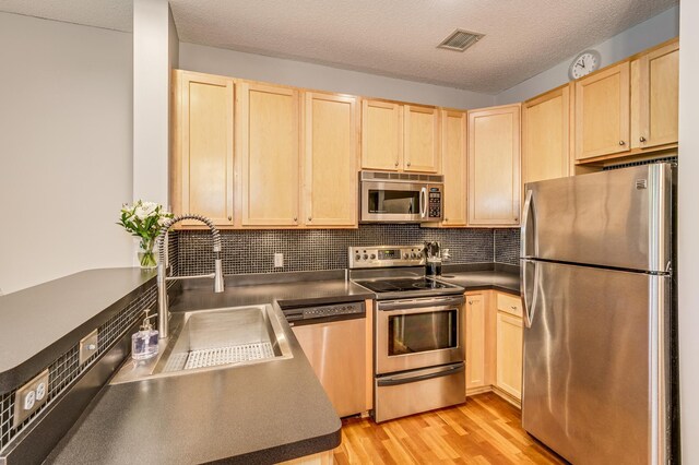 560 2nd St Unit 114, Minneapolis, MN 55401 - kitchen with appliances with stainless steel finishes, light brown cabinets, dark countertops, decorative backsplash, and a textured ceiling