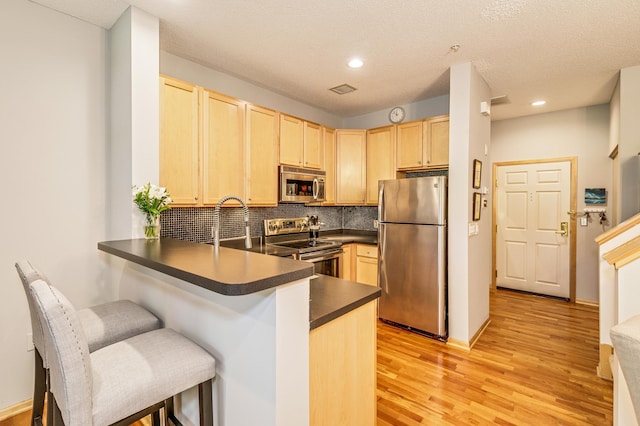 560 2nd St Unit 114, Minneapolis, MN 55401 - kitchen featuring appliances with stainless steel finishes, light brown cabinetry, dark countertops, a peninsula, and light wood-style floors
