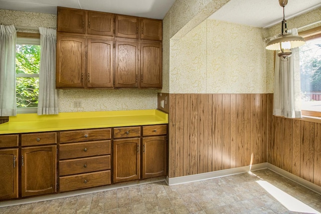 1700 Case Ave E, Saint Paul, MN 55106 - kitchen with brown cabinetry, light countertops, hanging light fixtures, wood walls, and baseboards