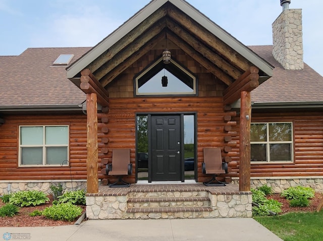 25712 15th Ave N, Highland Grove Twp, MN 56549 - view of exterior entry featuring log siding, roof with shingles, and covered porch