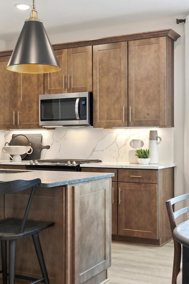 10635 Ithaca Ln N, Maple Grove, MN 55369 - kitchen with appliances with stainless steel finishes, light wood-type flooring, decorative backsplash, decorative light fixtures, and a kitchen bar