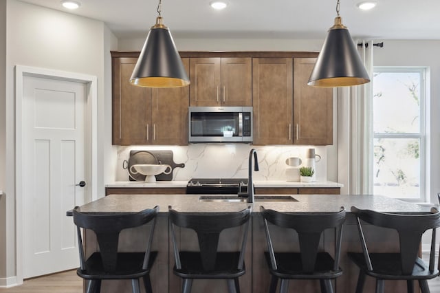 10635 Ithaca Ln N, Maple Grove, MN 55369 - kitchen with stainless steel microwave, a sink, decorative backsplash, decorative light fixtures, and a kitchen island with sink