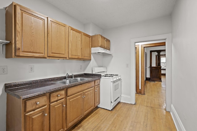 3400 Elliot Ave S, Minneapolis, MN 55407 - kitchen with white range with gas stovetop, a sink, under cabinet range hood, dark countertops, and light wood-style flooring