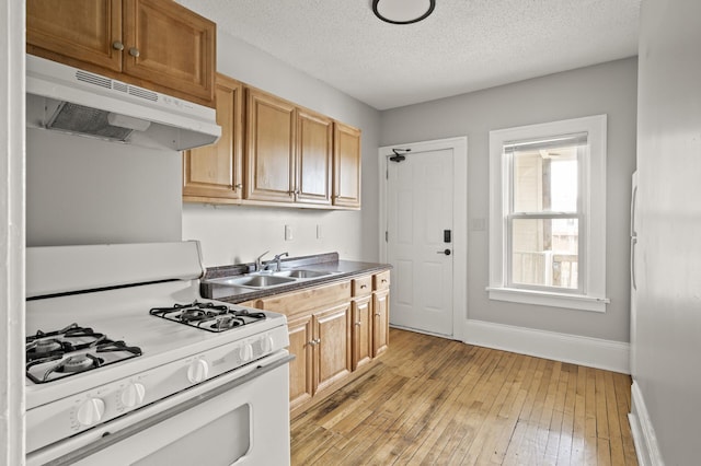 3400 Elliot Ave S, Minneapolis, MN 55407 - kitchen with white range with gas stovetop, under cabinet range hood, light wood finished floors, baseboards, and a textured ceiling