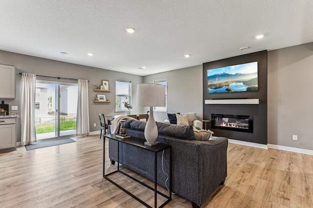 12719 Erskin St NE, Blaine, MN 55449 - living area featuring light wood finished floors, a textured ceiling, baseboards, a glass covered fireplace, and recessed lighting