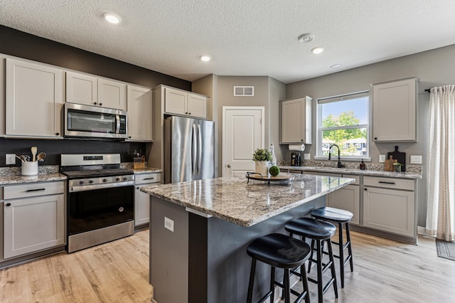 12719 Erskin St NE, Blaine, MN 55449 - kitchen featuring stainless steel appliances, light wood-type flooring, a kitchen breakfast bar, a kitchen island, and a textured ceiling