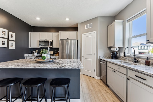 12719 Erskin St NE, Blaine, MN 55449 - kitchen with appliances with stainless steel finishes, a sink, a kitchen breakfast bar, light wood-style flooring, and light stone countertops