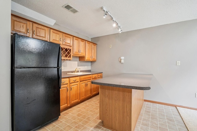 1504 Monarch St, Shakopee, MN 55379 - kitchen with freestanding refrigerator, a peninsula, a textured ceiling, track lighting, and dark countertops