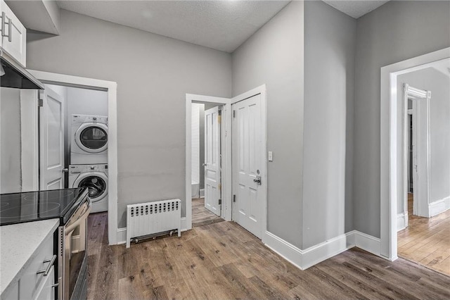 608 Beaumont St, Saint Paul, MN 55130 - laundry room with radiator heating unit, stacked washer and clothes dryer, dark wood-type flooring, and baseboards