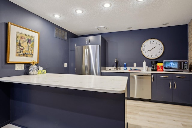 5697 Green Circle Dr Unit 216, Minnetonka, MN 55343 - kitchen featuring stainless steel appliances, a sink, a peninsula, a textured ceiling, and light wood-type flooring