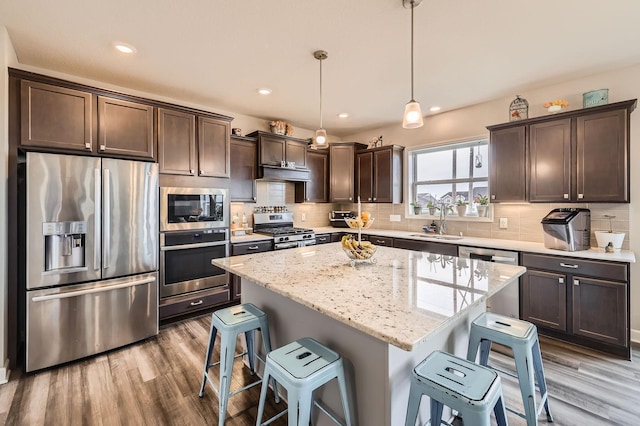 9602 7th St N, Lake Elmo, MN 55042 - kitchen featuring appliances with stainless steel finishes, dark brown cabinetry, a breakfast bar area, under cabinet range hood, and wood finished floors
