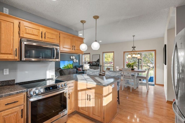 1107 Golden Way NW, Isanti, MN 55040 - kitchen featuring stainless steel appliances, a peninsula, light wood-style flooring, dark countertops, and hanging light fixtures