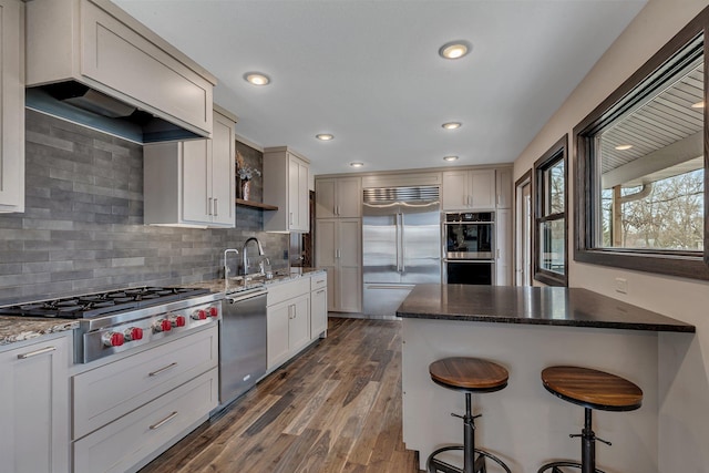 10267 Ferry Point Pl NW, Watab Twp, MN 56367 - kitchen featuring appliances with stainless steel finishes, a kitchen breakfast bar, dark stone countertops, backsplash, and dark wood-style flooring