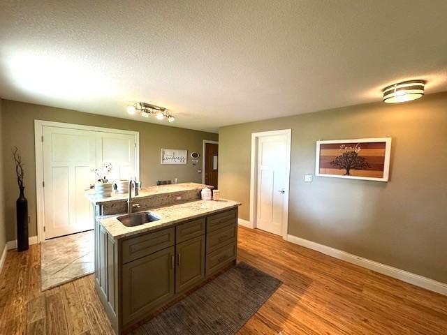 208 Mason Ave, Verndale, MN 56481 - kitchen with a sink, a center island with sink, light wood-style floors, baseboards, and a textured ceiling