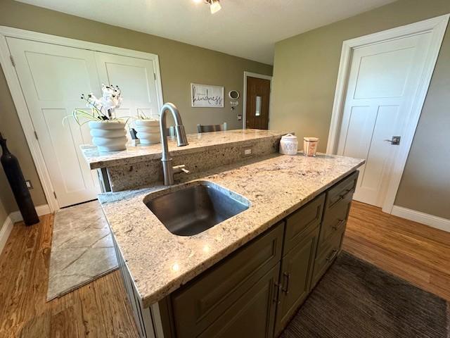 208 Mason Ave, Verndale, MN 56481 - kitchen featuring a sink, light wood-style floors, baseboards, light stone countertops, and an island with sink