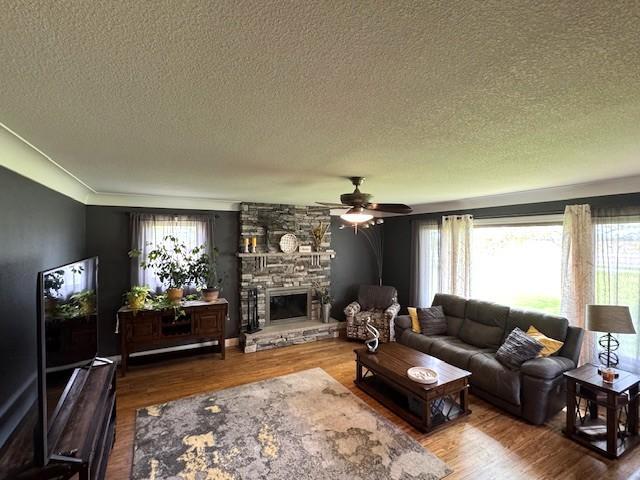 208 Mason Ave, Verndale, MN 56481 - living area featuring a textured ceiling, ceiling fan, a stone fireplace, and wood finished floors