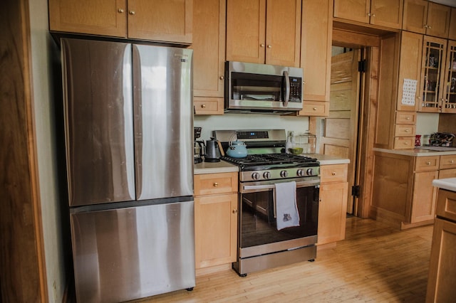 210 6th St, Morris, MN 56267 - kitchen featuring appliances with stainless steel finishes, light countertops, light wood-style floors, and glass insert cabinets