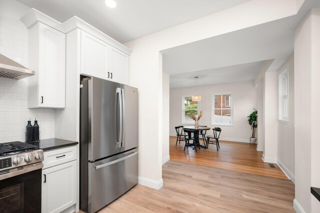 1836 Marshall Ave, Saint Paul, MN 55104 - kitchen featuring appliances with stainless steel finishes, decorative backsplash, white cabinetry, light wood finished floors, and wall chimney range hood