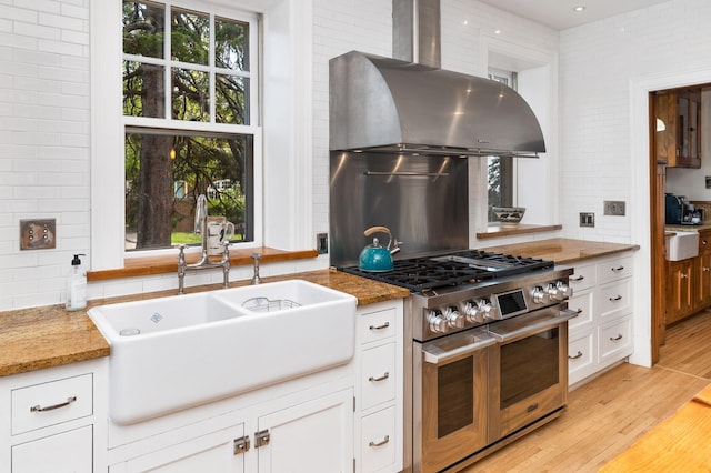 2525 2nd St, Duluth, MN 55812 - kitchen with range with two ovens, a sink, wall chimney exhaust hood, decorative backsplash, and white cabinetry