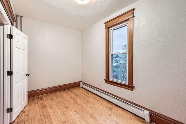 1156 Marion St, Saint Paul, MN 55117 - empty room with a baseboard heating unit, light wood-style floors, a textured wall, and baseboards