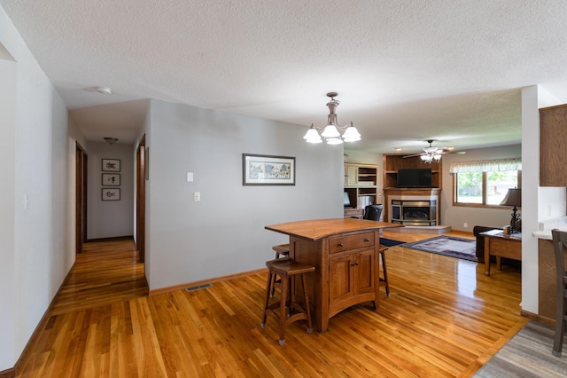 32 7th St, Buffalo City, WI 54622 - dining area featuring light wood finished floors, a fireplace with raised hearth, a textured ceiling, a chandelier, and a ceiling fan