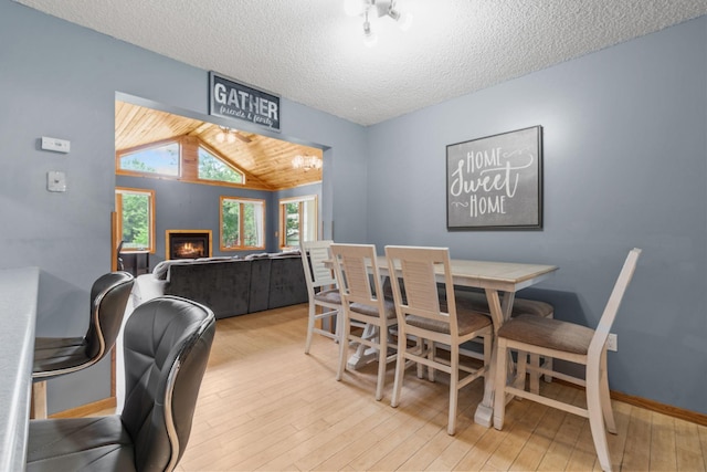 16724 Kenyon Cir NE, Ham Lake, MN 55304 - dining area featuring a lit fireplace, lofted ceiling, light wood-style flooring, and a textured ceiling