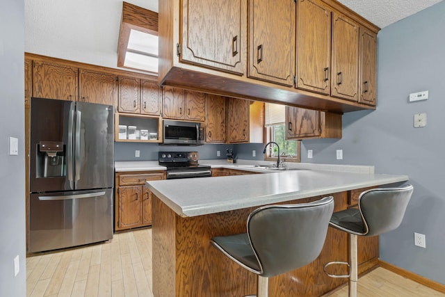 16724 Kenyon Cir NE, Ham Lake, MN 55304 - kitchen featuring appliances with stainless steel finishes, brown cabinetry, a peninsula, light countertops, and light wood-type flooring
