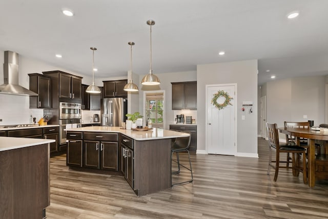 19281 Blue Stem Ct, Maple Grove, MN 55311 - kitchen featuring wall chimney exhaust hood, appliances with stainless steel finishes, light countertops, dark brown cabinets, and wood finished floors