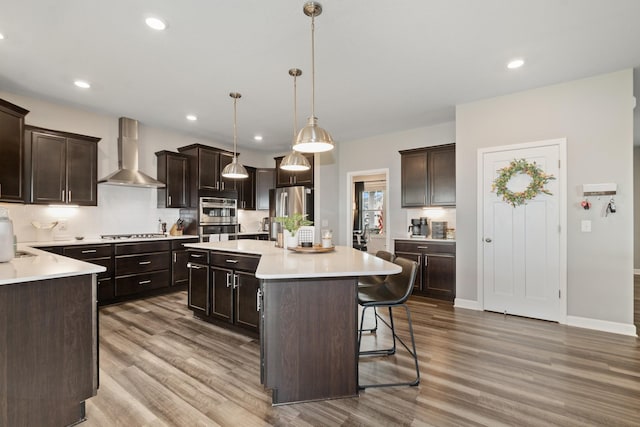 19281 Blue Stem Ct, Maple Grove, MN 55311 - kitchen with wall chimney exhaust hood, wood finished floors, dark brown cabinets, a center island, and recessed lighting
