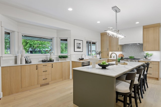 2324 Rivendell Ln, Minnetonka, MN 55305 - kitchen with light brown cabinetry, decorative backsplash, a kitchen island with sink, a kitchen bar, and light wood-style floors
