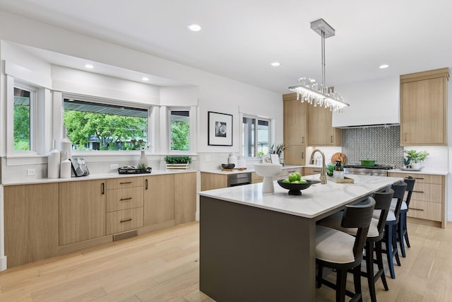 2324 Rivendell Ln, Minnetonka, MN 55305 - kitchen with decorative backsplash, light brown cabinetry, a center island with sink, a kitchen bar, and recessed lighting