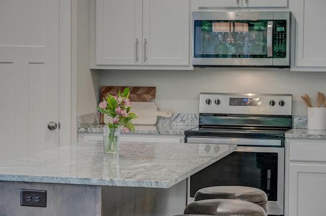 1345 Bluff Border Rd, New Richmond, WI 54017 - kitchen with stainless steel appliances, white cabinetry, light stone countertops, a breakfast bar area, and a center island