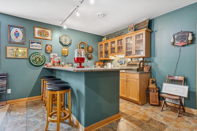 26033 607th St, Mantorville, MN 55955 - kitchen featuring a breakfast bar area, track lighting, stone tile flooring, glass insert cabinets, and a peninsula