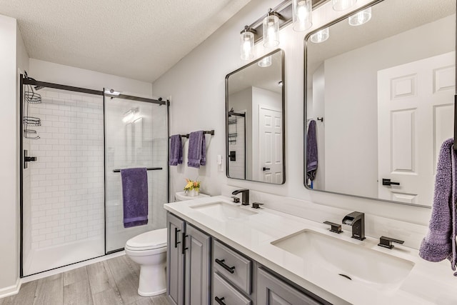 11001 Isanti Ct NE, Blaine, MN 55449 - bathroom featuring a textured ceiling, double vanity, a stall shower, toilet, and wood finished floors