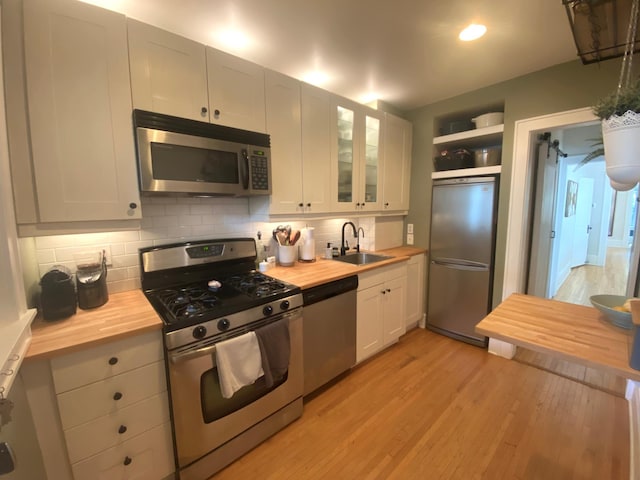 3112 Bryant Ave S Unit 1, Minneapolis, MN 55408 - kitchen with appliances with stainless steel finishes, wood counters, a sink, light wood finished floors, and tasteful backsplash