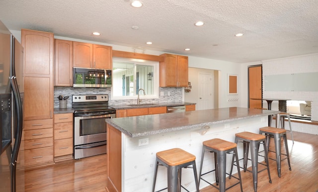 2603 140th Ln NW, Andover, MN 55304 - kitchen featuring stainless steel appliances, light wood finished floors, a textured ceiling, a kitchen island, and a breakfast bar
