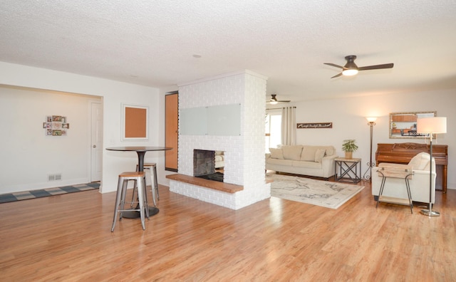2603 140th Ln NW, Andover, MN 55304 - living area featuring light wood-style flooring, a textured ceiling, a ceiling fan, and a brick fireplace