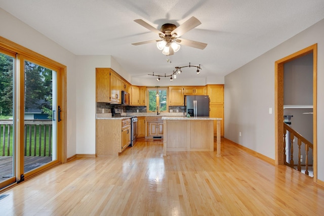 7811 209th St N, Forest Lake, MN 55025 - kitchen with appliances with stainless steel finishes, light wood-style floors, a kitchen island, decorative backsplash, and a ceiling fan