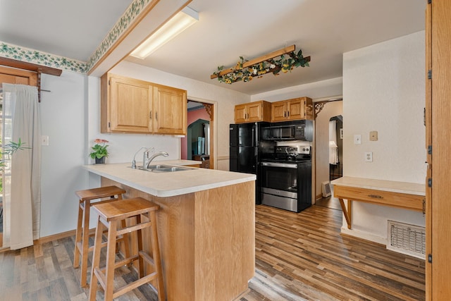 308 4th Ave SW, Austin, MN 55912 - kitchen with black appliances, a sink, wood finished floors, a breakfast bar, and a peninsula