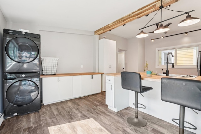 491 Belvidere St E, Saint Paul, MN 55107 - kitchen with wood counters, stacked washer and clothes dryer, wood finished floors, white cabinets, and a kitchen breakfast bar