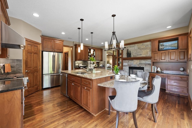 8867 Aviary Path, Inver Grove Heights, MN 55077 - kitchen featuring stainless steel appliances, wall chimney exhaust hood, a kitchen island with sink, a sink, and dark wood-style floors