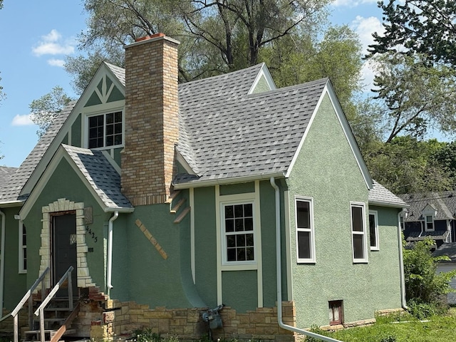 view of front of house with entry steps, stucco siding, a chimney, and a shingled roof