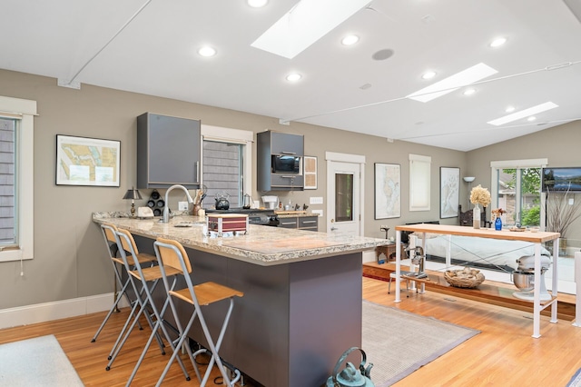 475 Lakeview Ave, Tonka Bay, MN 55331 - kitchen with a skylight, gray cabinetry, light wood-style floors, a breakfast bar, and a peninsula