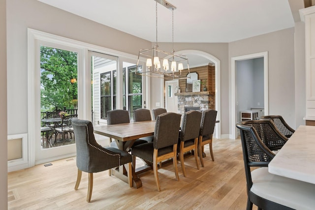 1432 25th St, Saint Joseph Twp, WI 54082 - dining space with light wood-style floors, a chandelier, a stone fireplace, and arched walkways