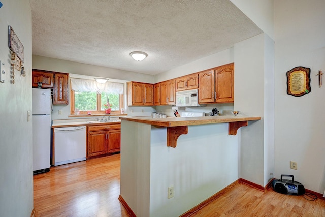 106 4th Ave NW, Rice, MN 56367 - kitchen with white appliances, light wood-type flooring, a breakfast bar, brown cabinetry, and a peninsula