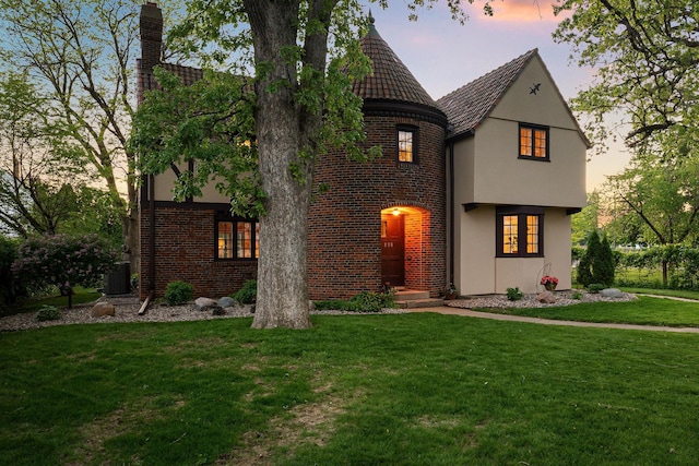 808 4th St SW, Austin, MN 55912 - tudor-style house with a yard, brick siding, stucco siding, a chimney, and cooling unit